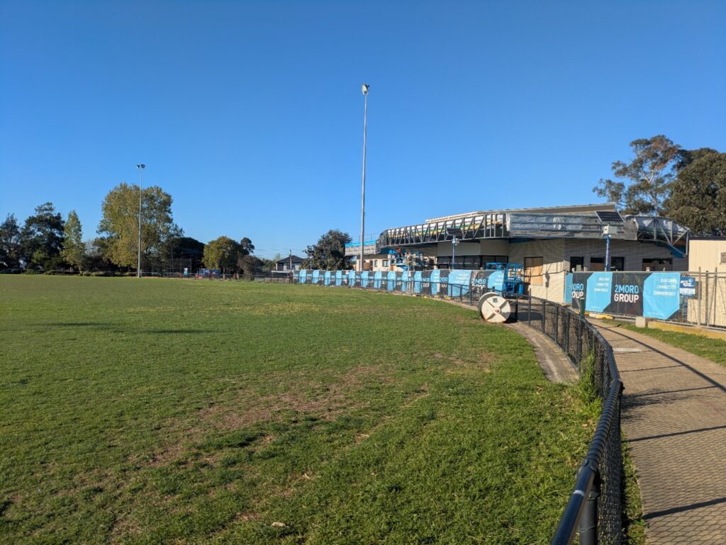 Path beside the oval and fenced pavilion building works at Mackie Reserve.