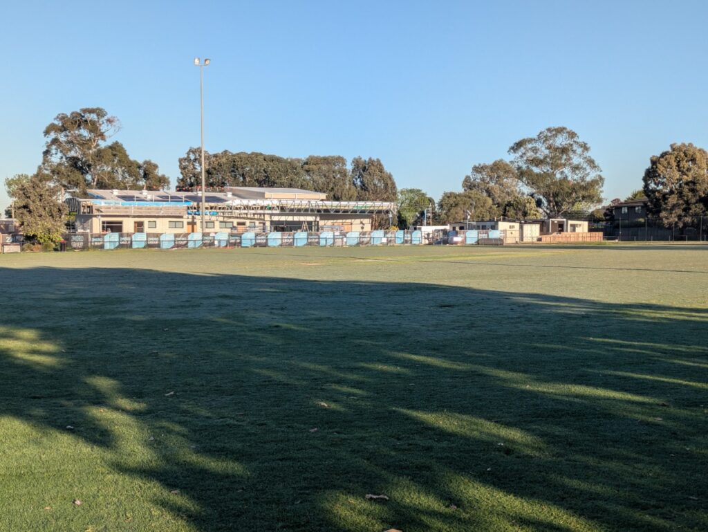 Mackie Reserve pavilion under redevelopment, viewed across the oval with construction fencing in front.